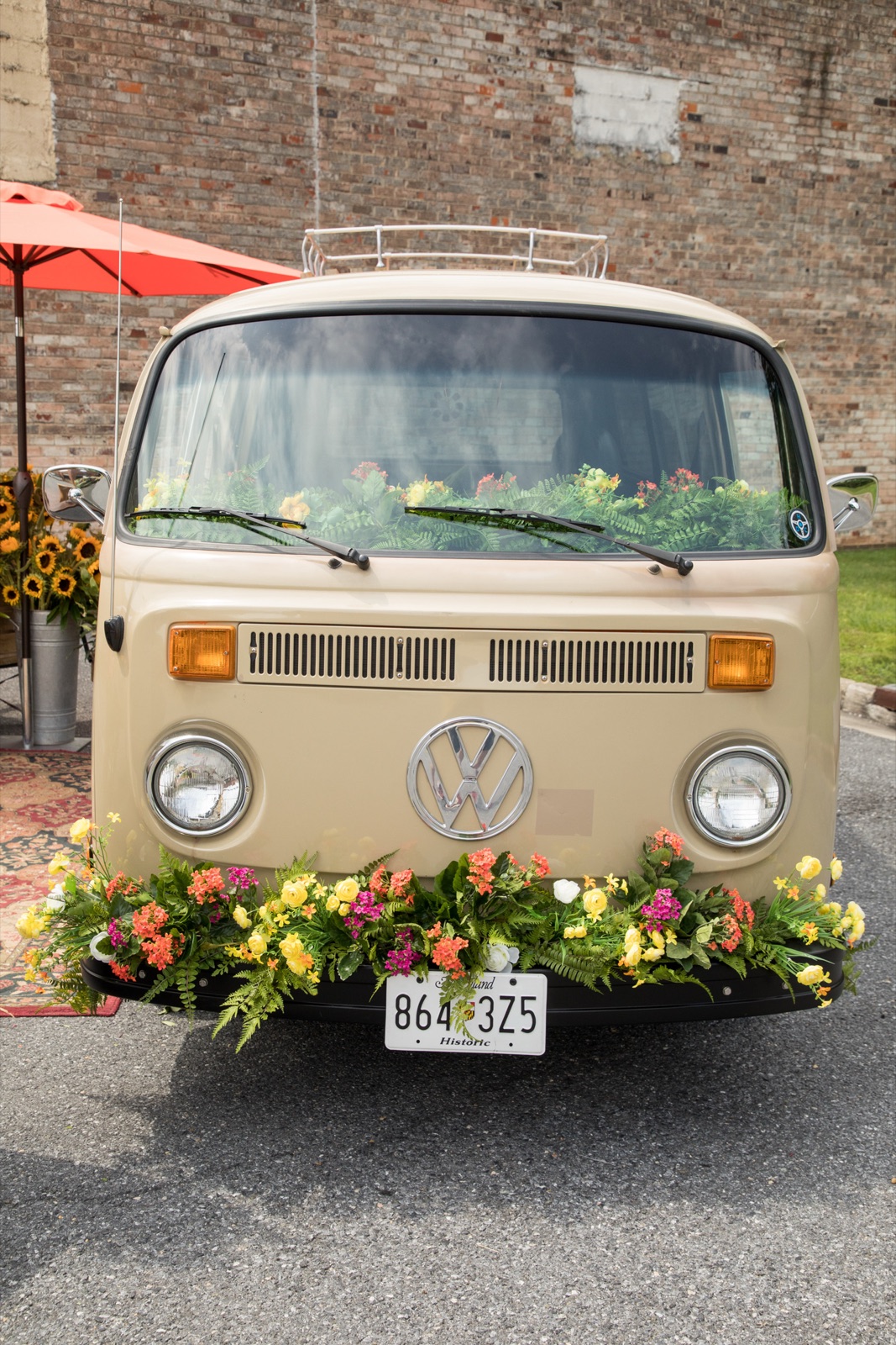 The VW Blooming Bus — cream 1979 Volkswagen decorated with colorful seasonal flowers across the front bumper, parked in front of a brick wall